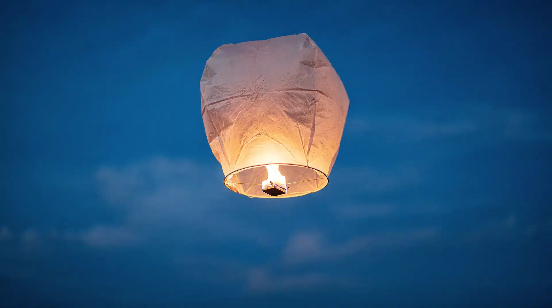 Lampion volant en papier blanc s'élevant dans un ciel bleu de fin de journée
